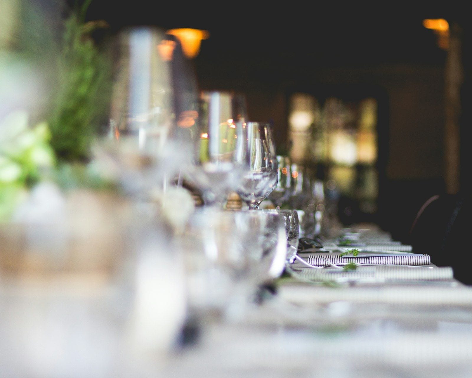 A long table set with glassware, candlelight and greenery for a private event